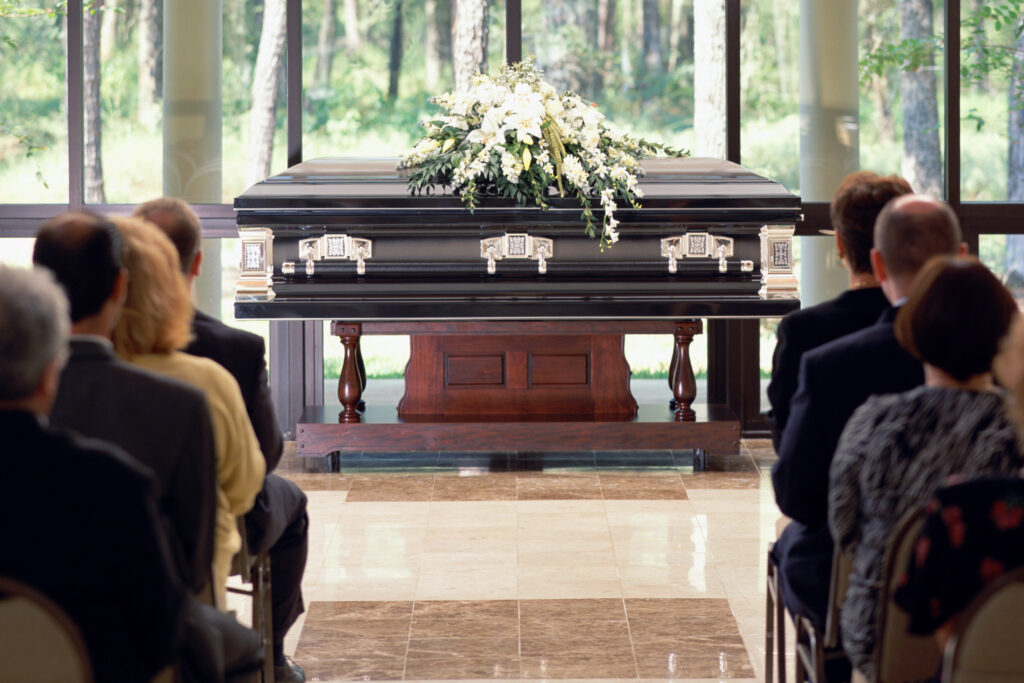 Group of people sitting at funeral, casket with flowers in front